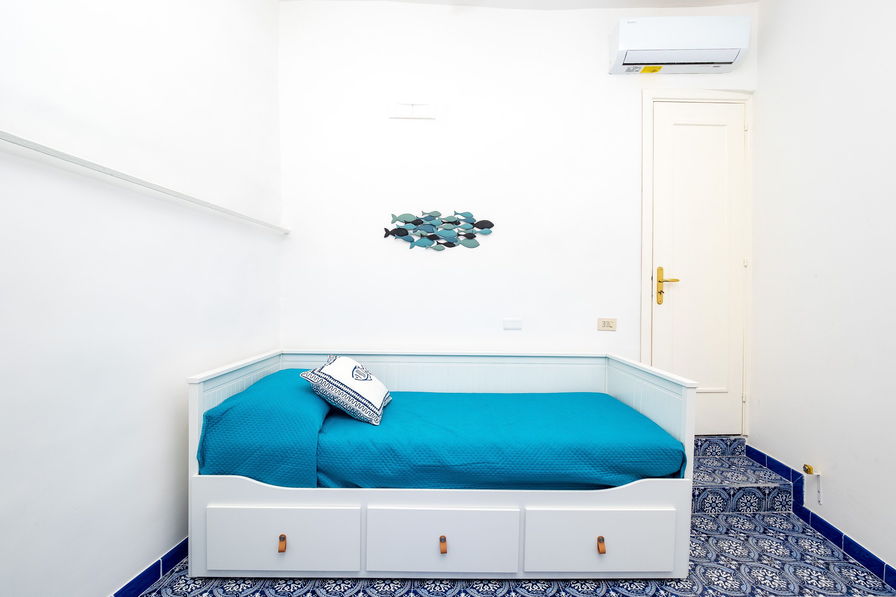 Ein Schlafzimmer mit einem weißen Bett, blauer Bettwäsche, einem gemusterten Boden und einer weißen Tür.