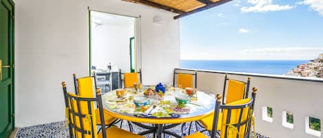 A round table with yellow chairs and a blue and white patterned floor, overlooking a coastal view.