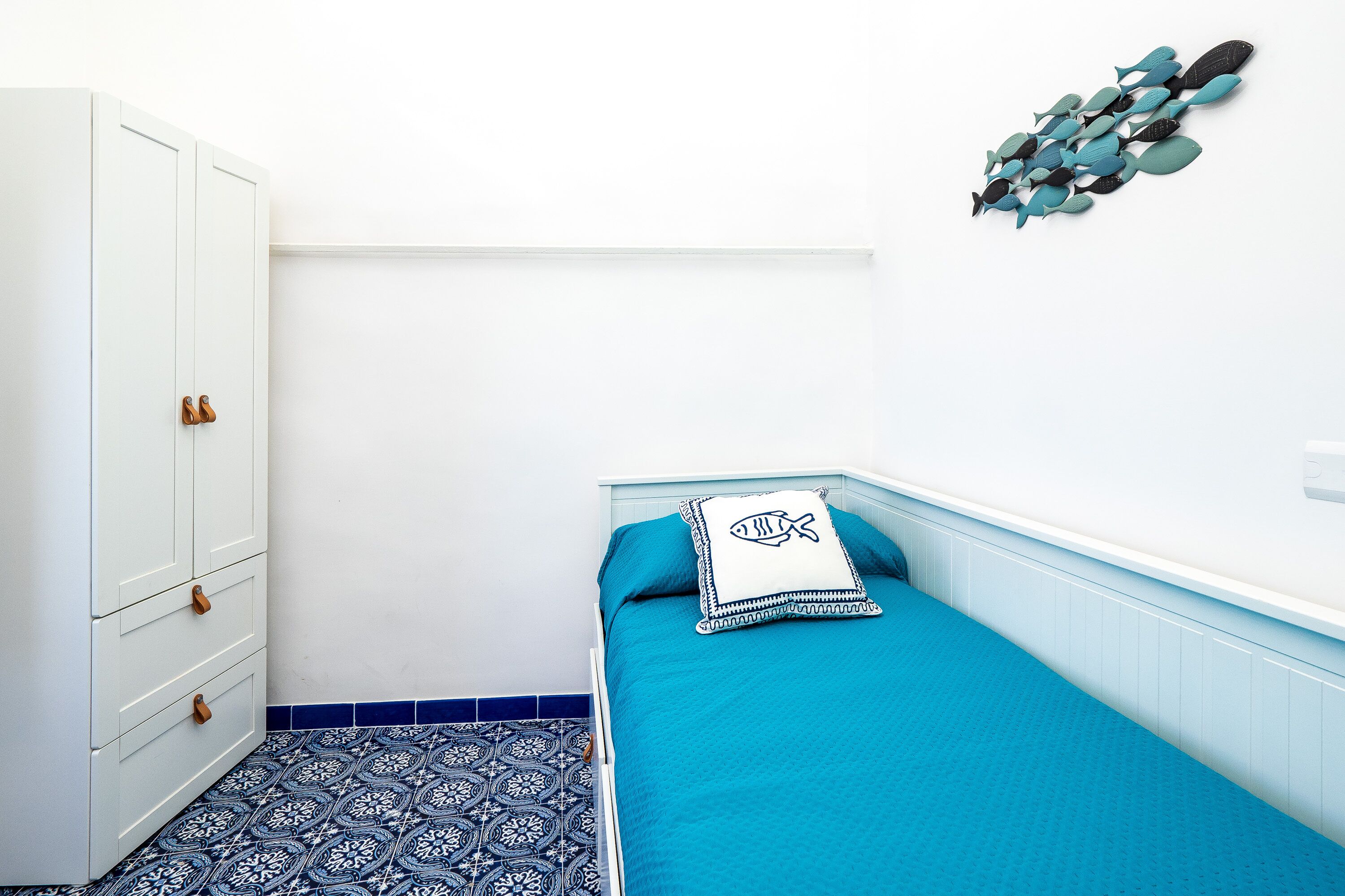 Une petite chambre à coucher, bien rangée, avec un lit, une armoire et une étagère fixée au mur.