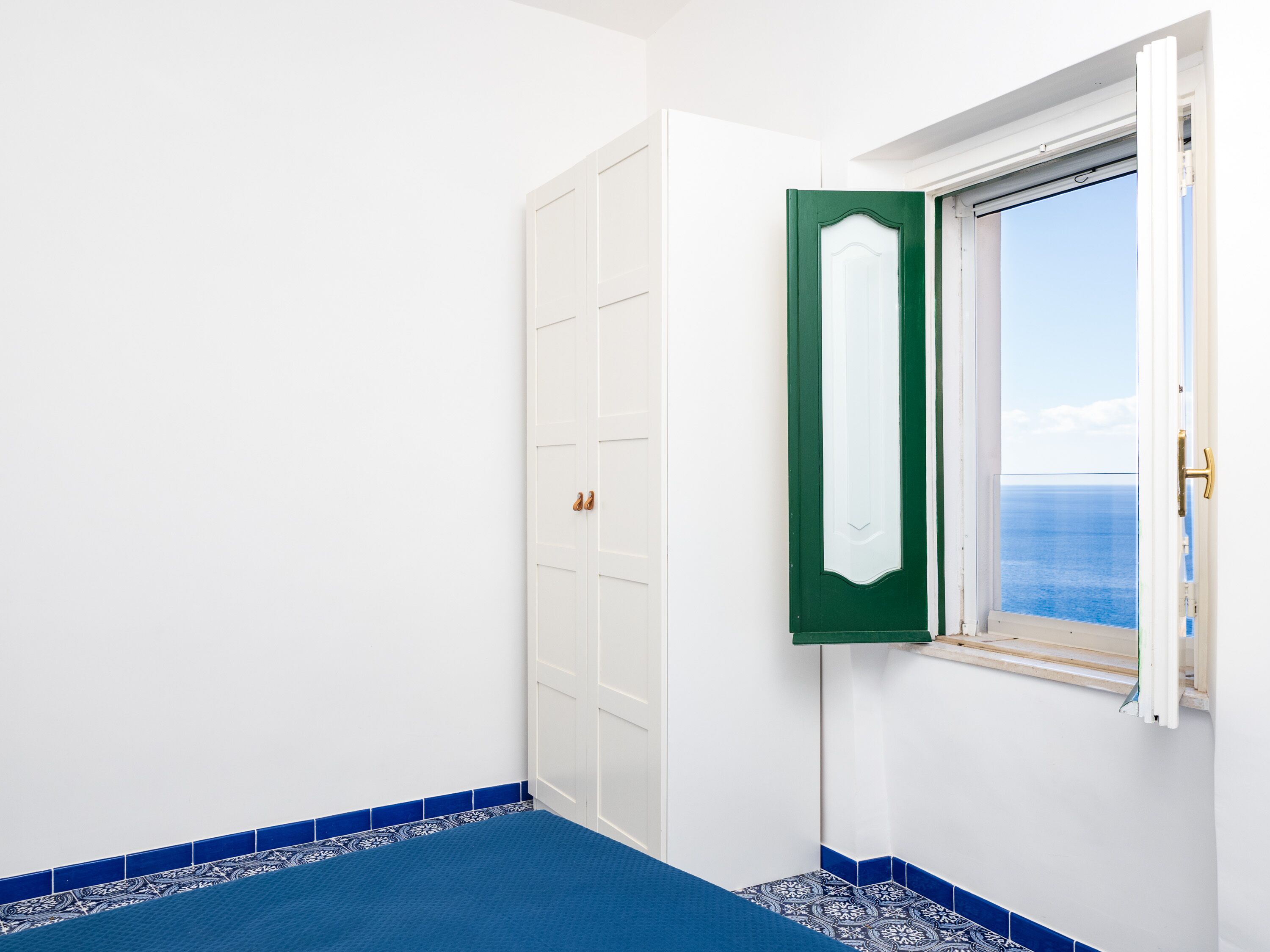 Una stanza con una porta bianca, un telaio di porta verde e una finestra con vista sul mare.