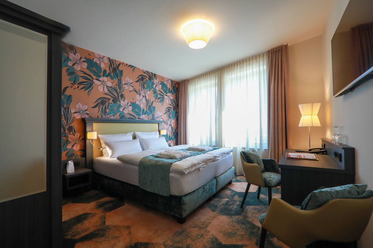 A hotel room with a large bed, a desk, a chair, and a TV.