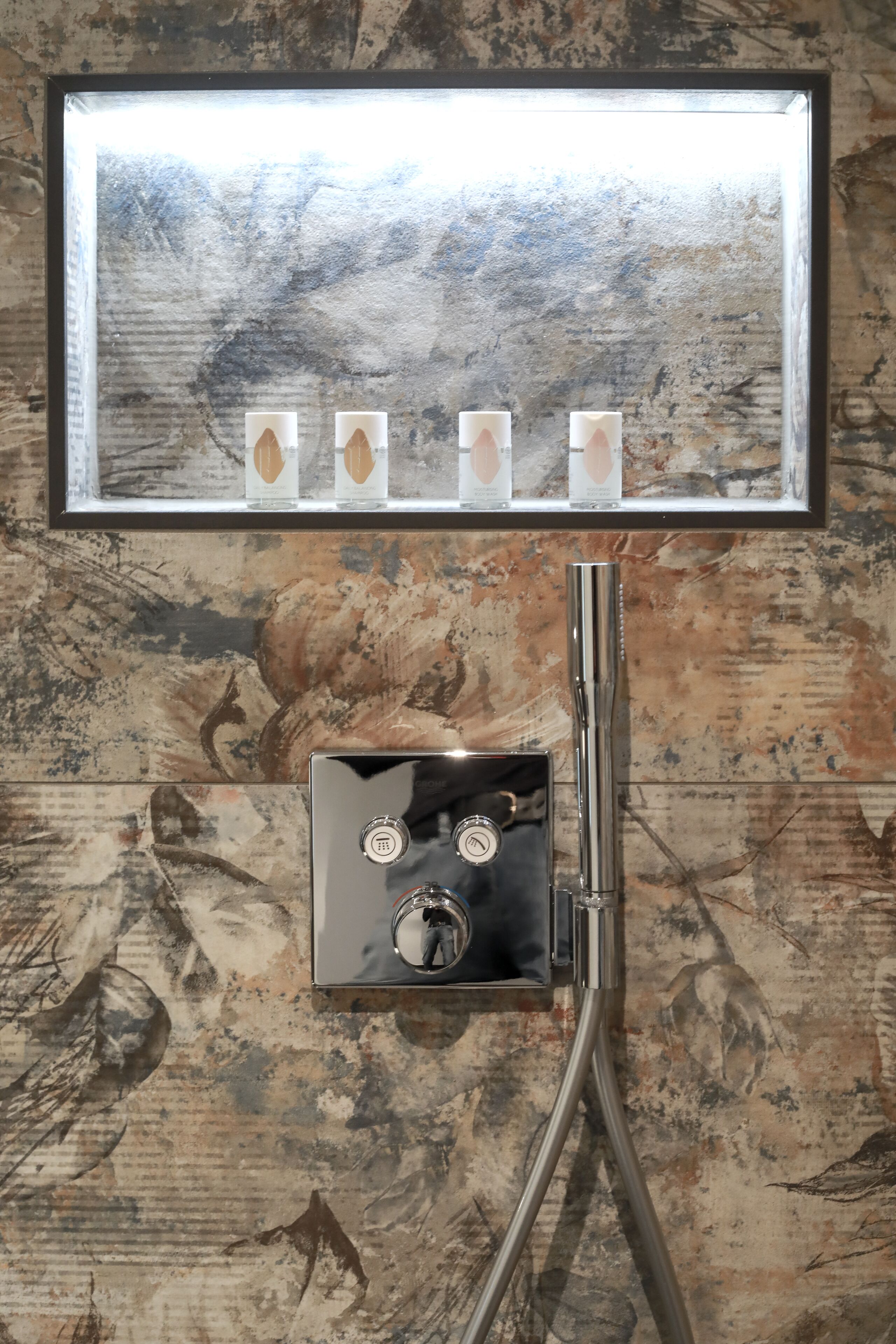 A bathroom with a large mirror, a shower with a control panel, and a decorative wall with a natural pattern.