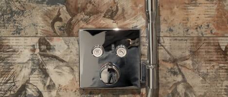 A bathroom with a large mirror, a shower with a control panel, and a decorative wall with a natural pattern.