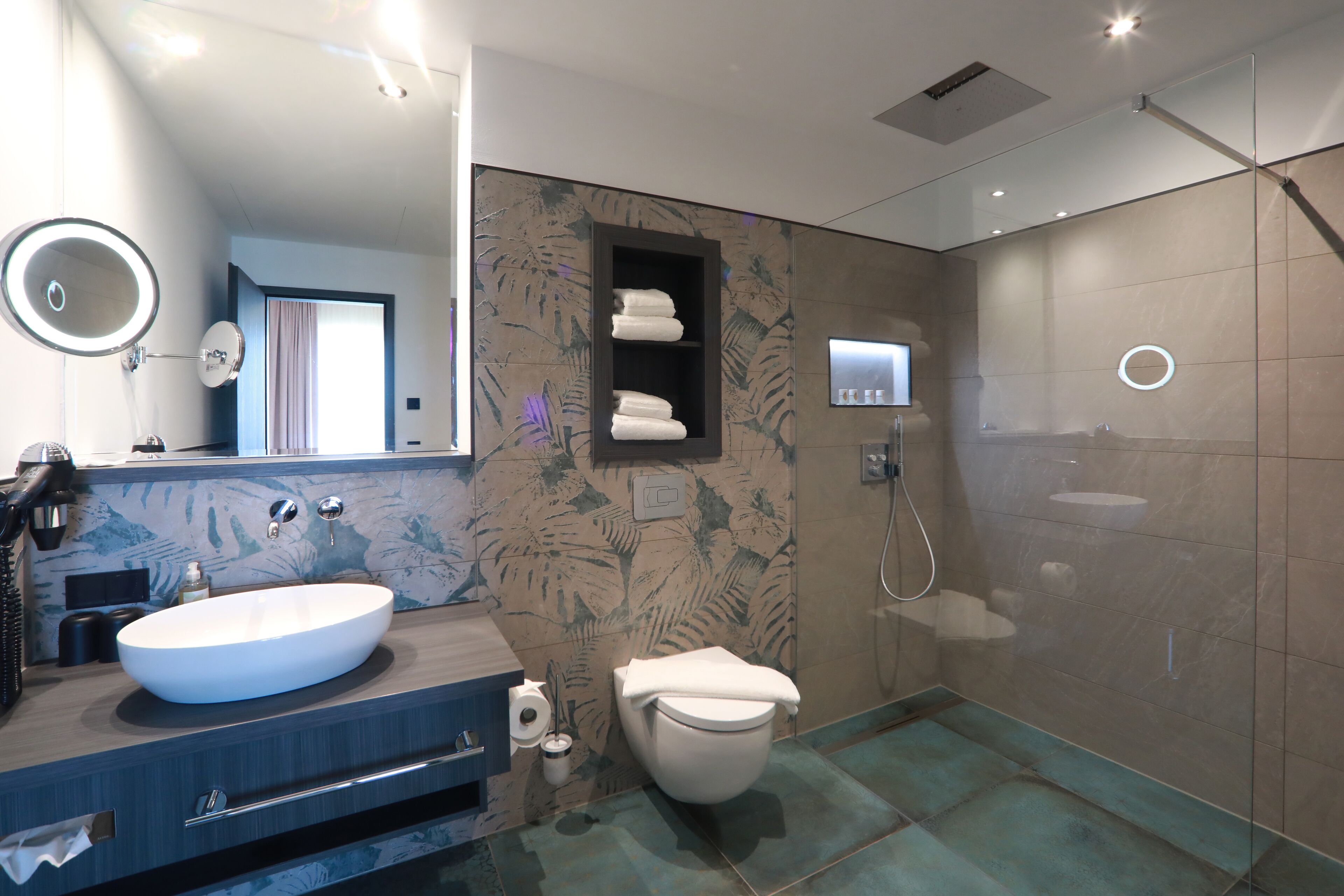 A modern bathroom with a large oval sink, a toilet, a shower, and a mirror with a light.