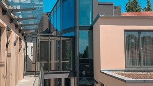 A modern building with a glass facade, a covered walkway, and a clear blue sky. - SPREE. Hotel am Hafen (Lübbenau/Spreewald)
