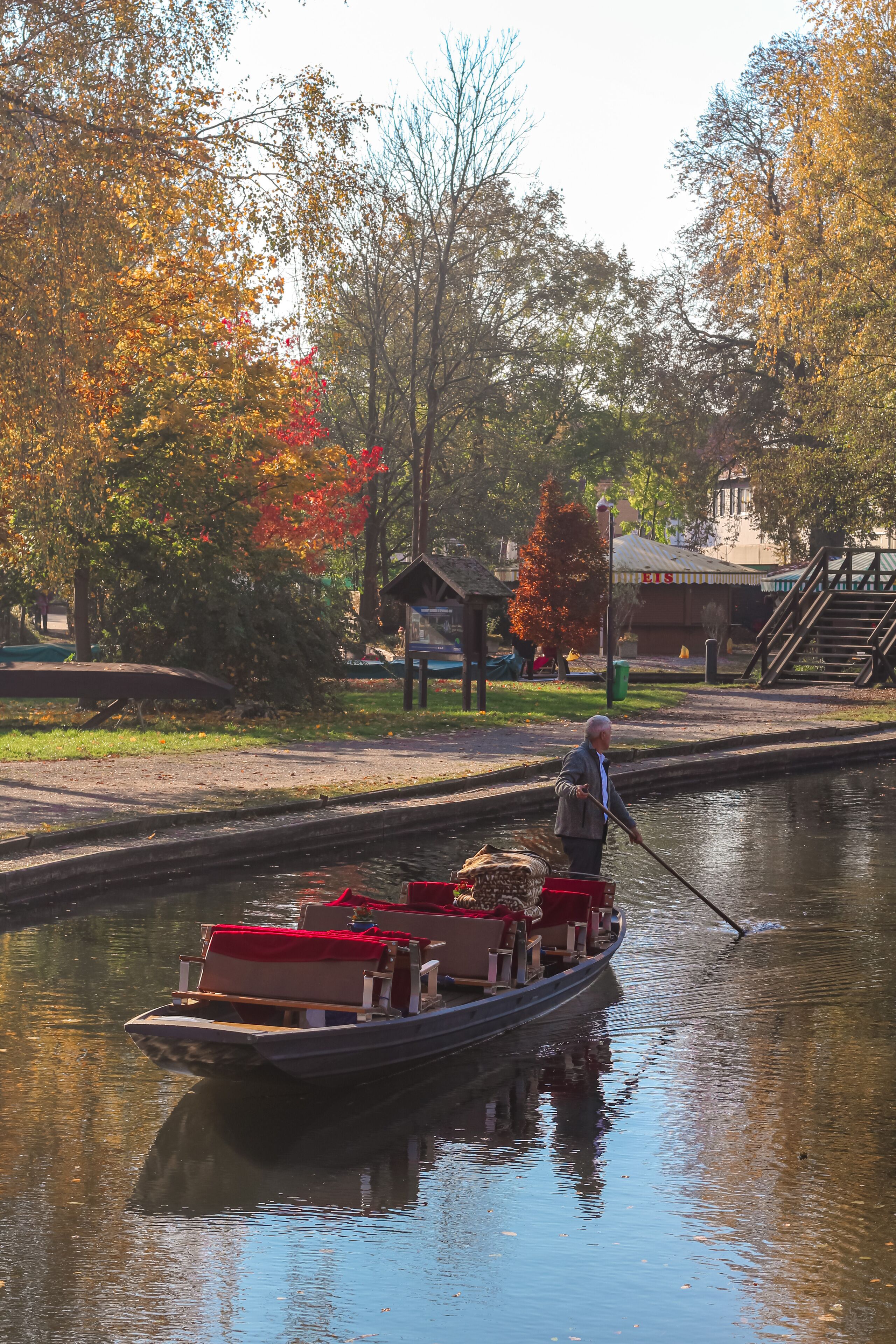 A narrow canal with a boat carrying wooden chairs and a red cover.