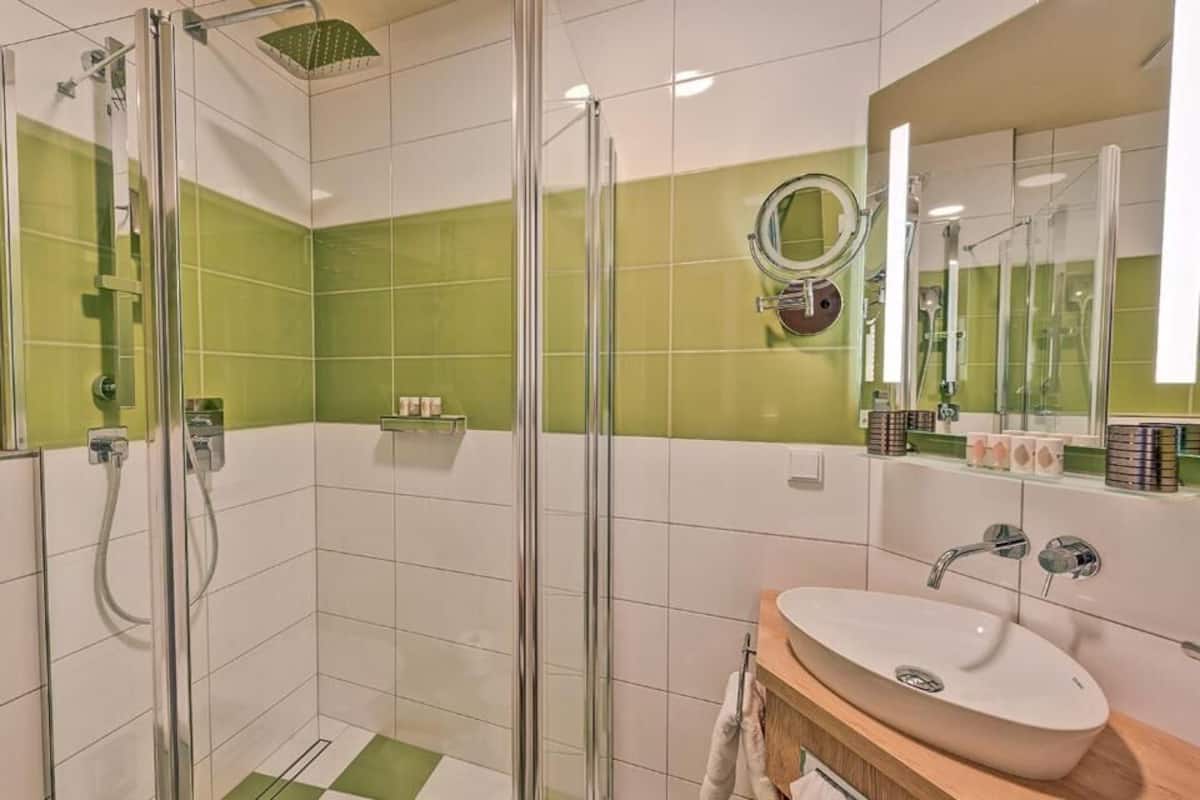 A bathroom with a glass-enclosed shower, a sink with a mirror, and green-tiled walls.