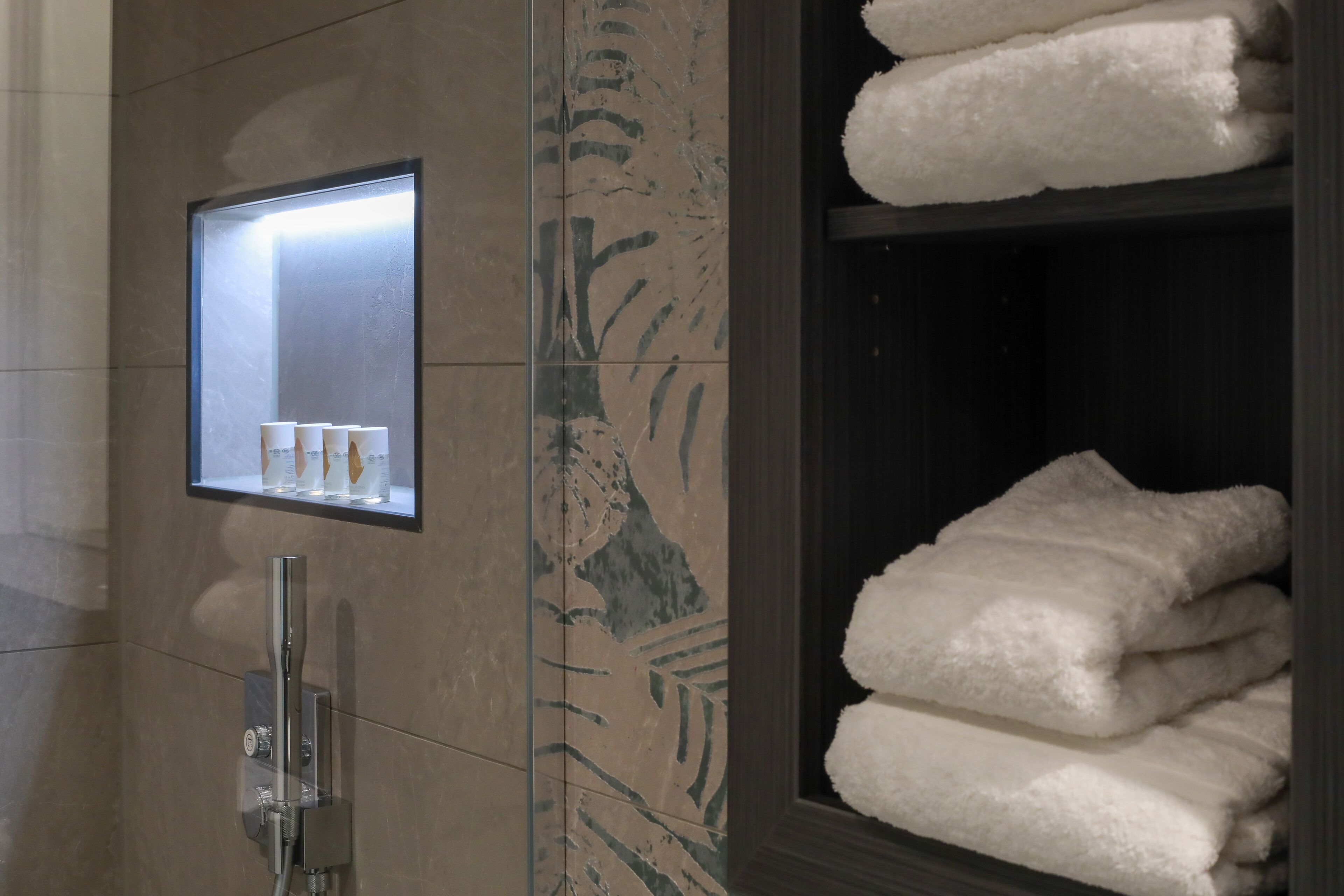 Un baño con cabina de ducha de vidrio, un perchero con toallas dobladas y un espejo con un cuadro enmarcado.