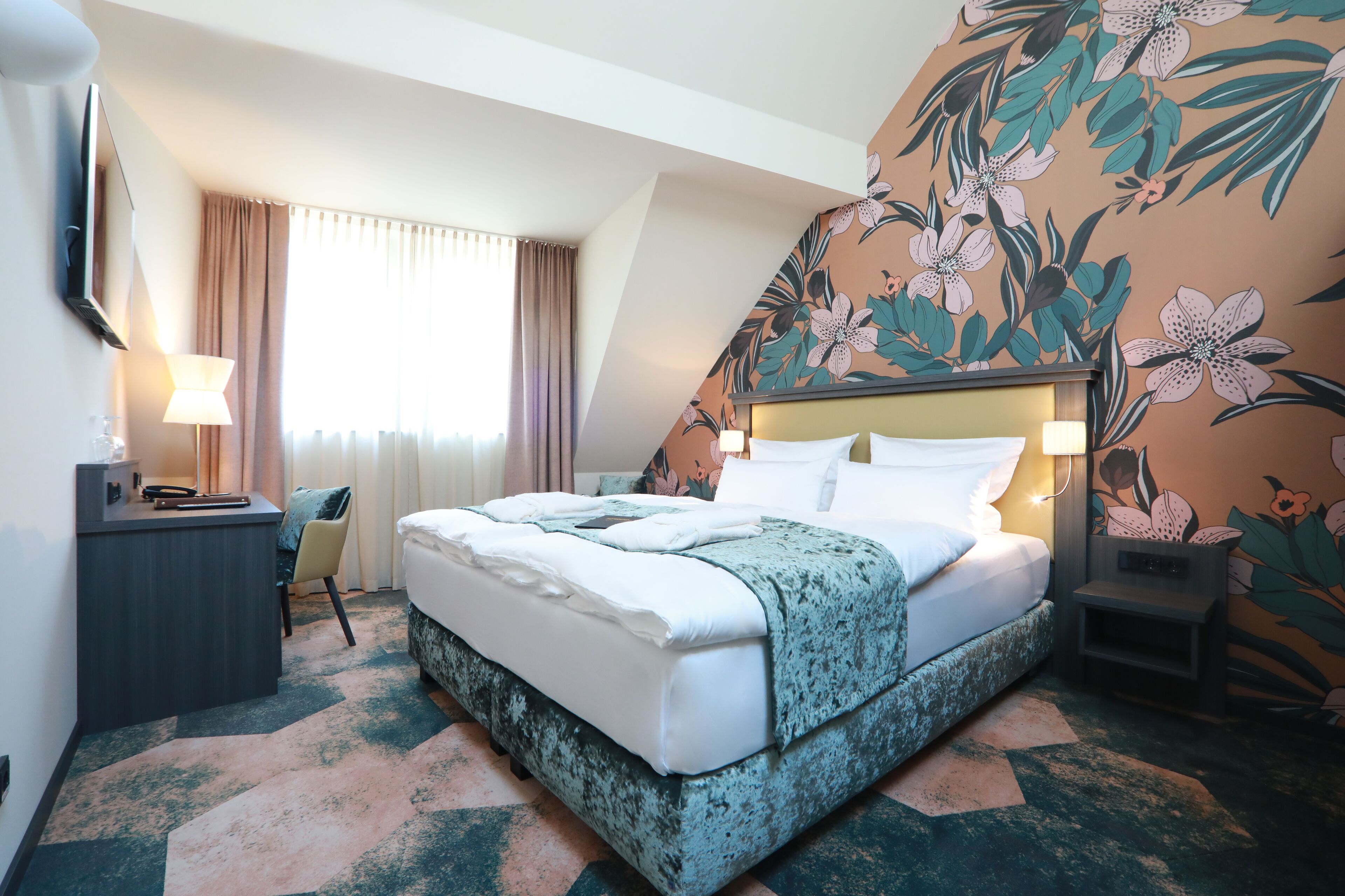 A hotel room with a bed, a desk, a chair, a TV, and a window with curtains.