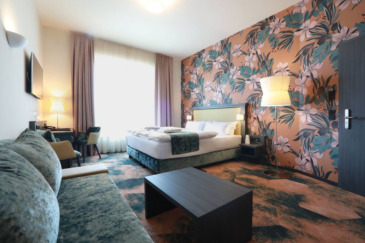 A hotel room with a bed, a sofa, a coffee table, a desk, and a lamp.