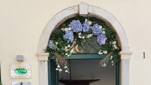 An entrance with a decorative archway adorned with flowers and greenery, a plaque with text, and a small table with a sign. - Torre A Mare Porto Venere (Portovenere)