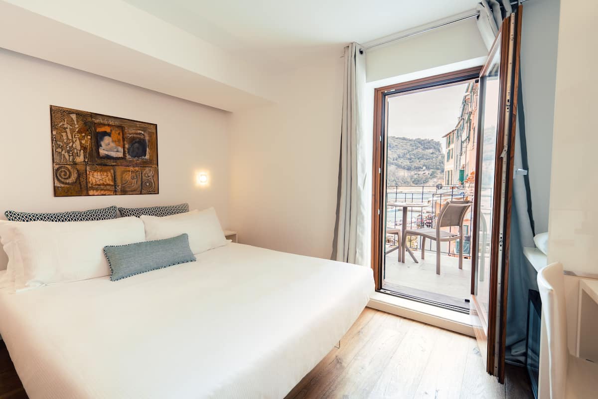 Une chambre à coucher avec un lit, un tableau au mur et une vue sur un balcon aménagé avec du mobilier d’extérieur.