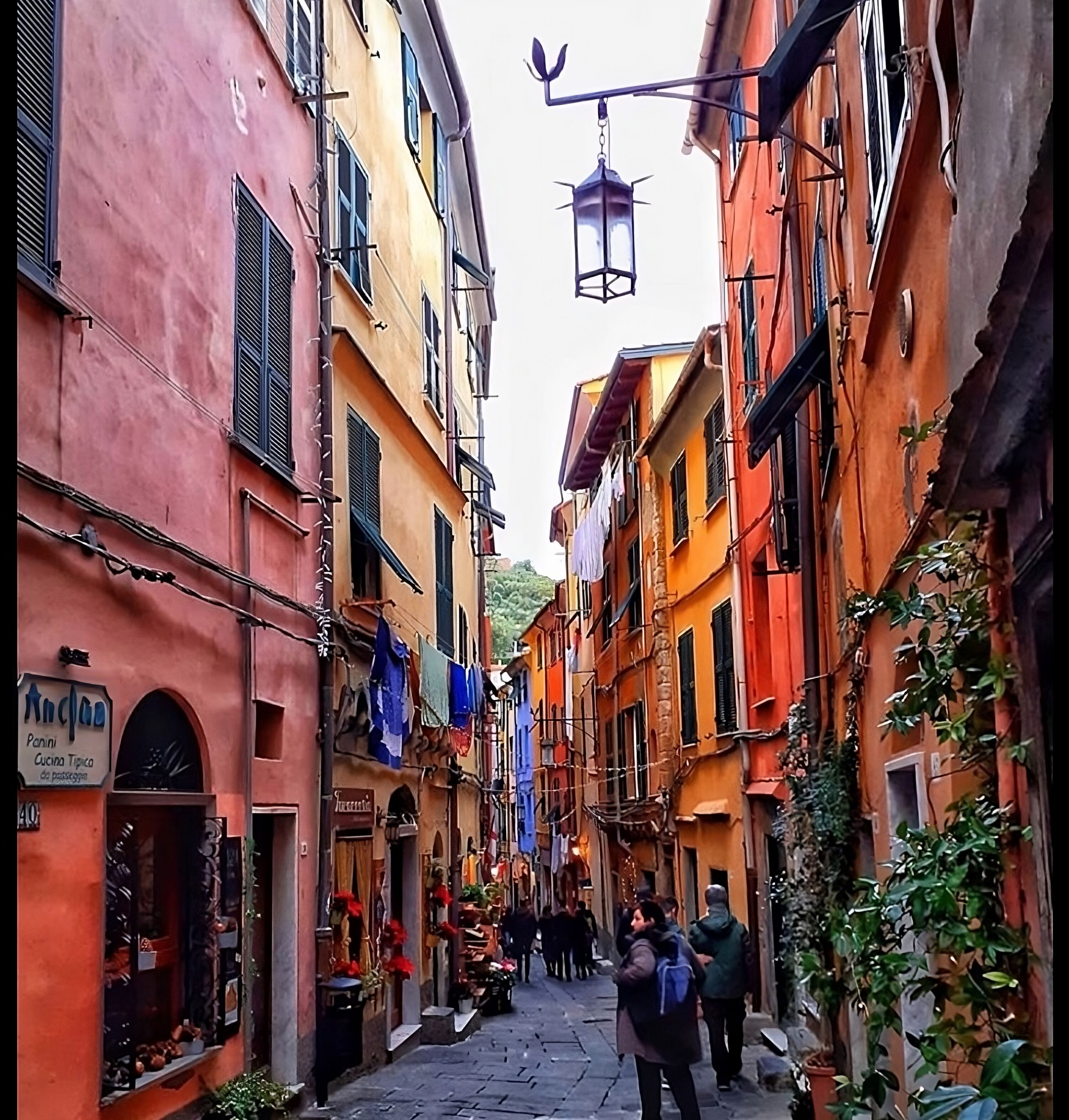 A narrow street with colorful buildings, a hanging lantern, and people walking.