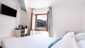 A hotel room with a bed, a desk, a TV, and a window with a view of a mountainous landscape. - Torre A Mare Porto Venere (Portovenere)