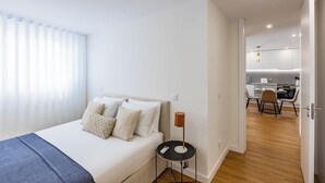 Un dormitorio moderno con cama, mesita de noche y vistas al área de la cocina.