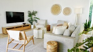 Un soggiorno moderno con una TV a schermo piatto, un mobile porta TV in legno, un tavolino rotondo, un divano e una poltrona in rattan.