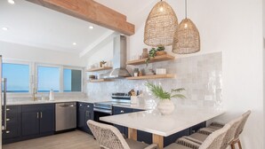Una cucina moderna con mobili scuri, un'isola bianca, sedie in vimini e luci a sospensione.