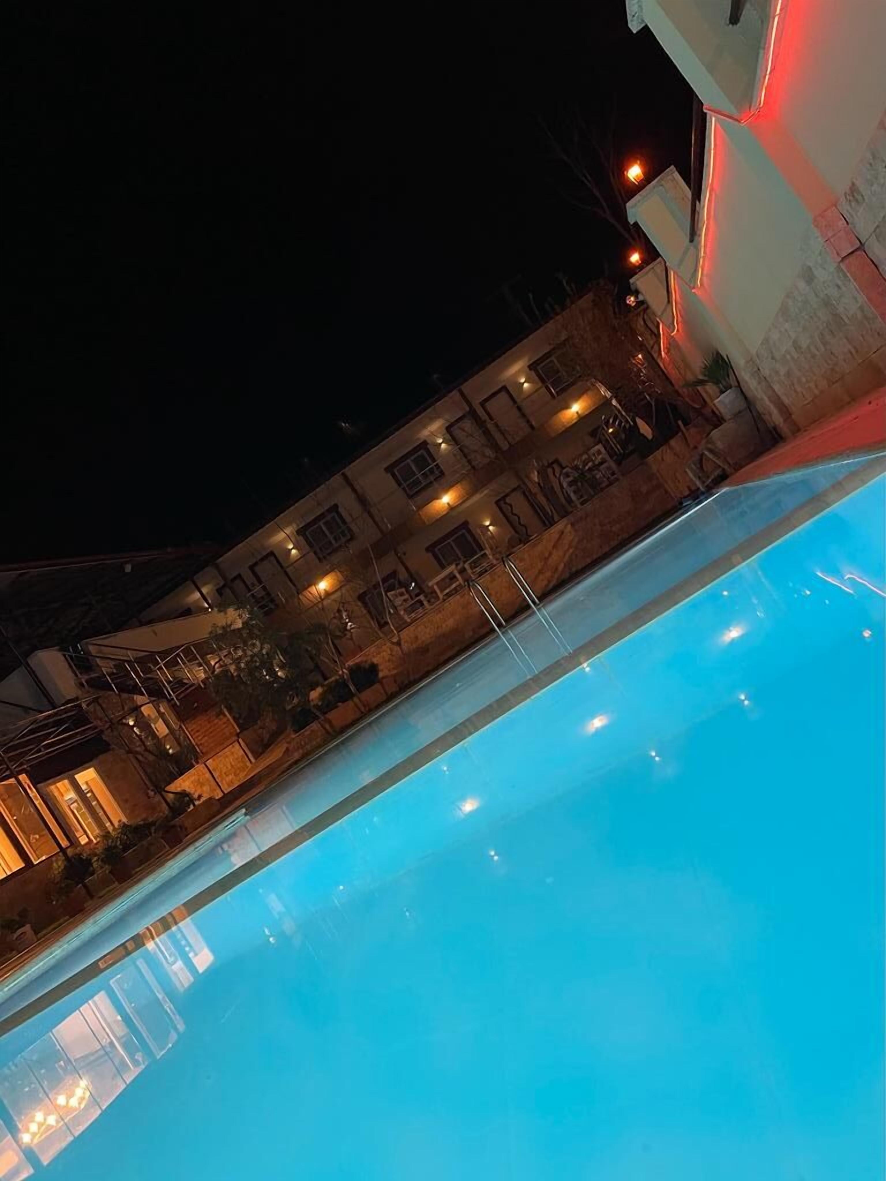 A swimming pool with a clear blue water surface, surrounded by a building with multiple windows and a stone facade.