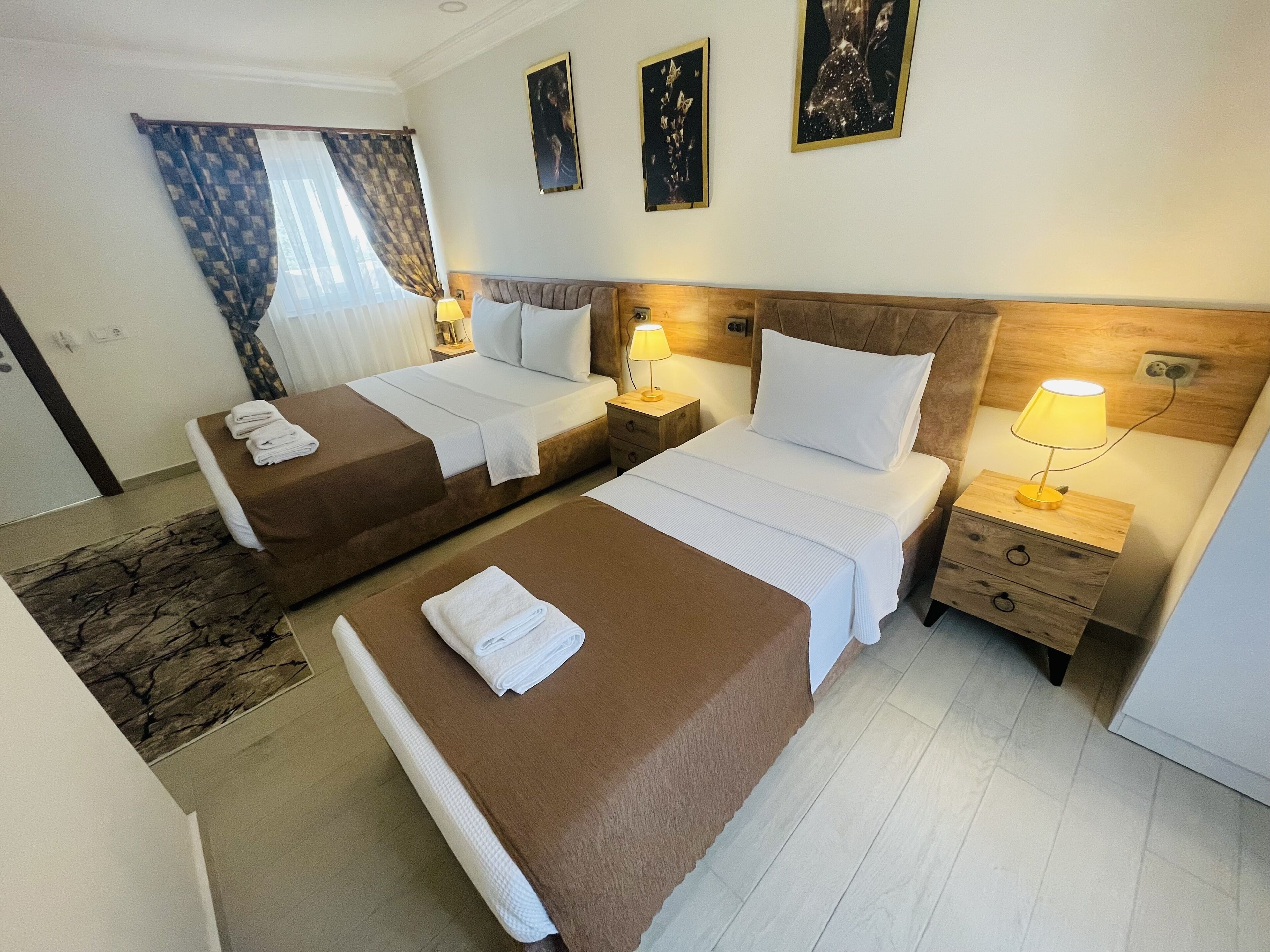 Une chambre d’hôtel avec deux lits, une tête de lit en bois, une table de chevet avec une lampe et une fenêtre avec des rideaux.