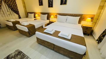 Quarto de hotel com duas camas, um espaço de estar e uma janela grande com cortinas.