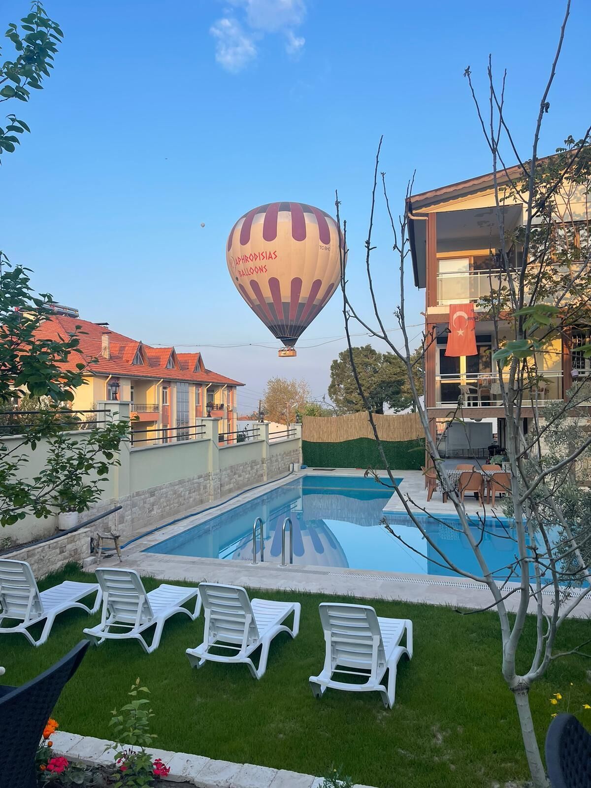 A swimming pool with lounge chairs, a hot air balloon in the background, and a building with a flag.