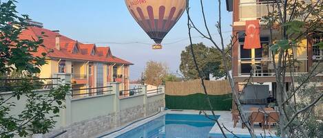 A swimming pool with lounge chairs, a hot air balloon in the background, and a building with a flag.