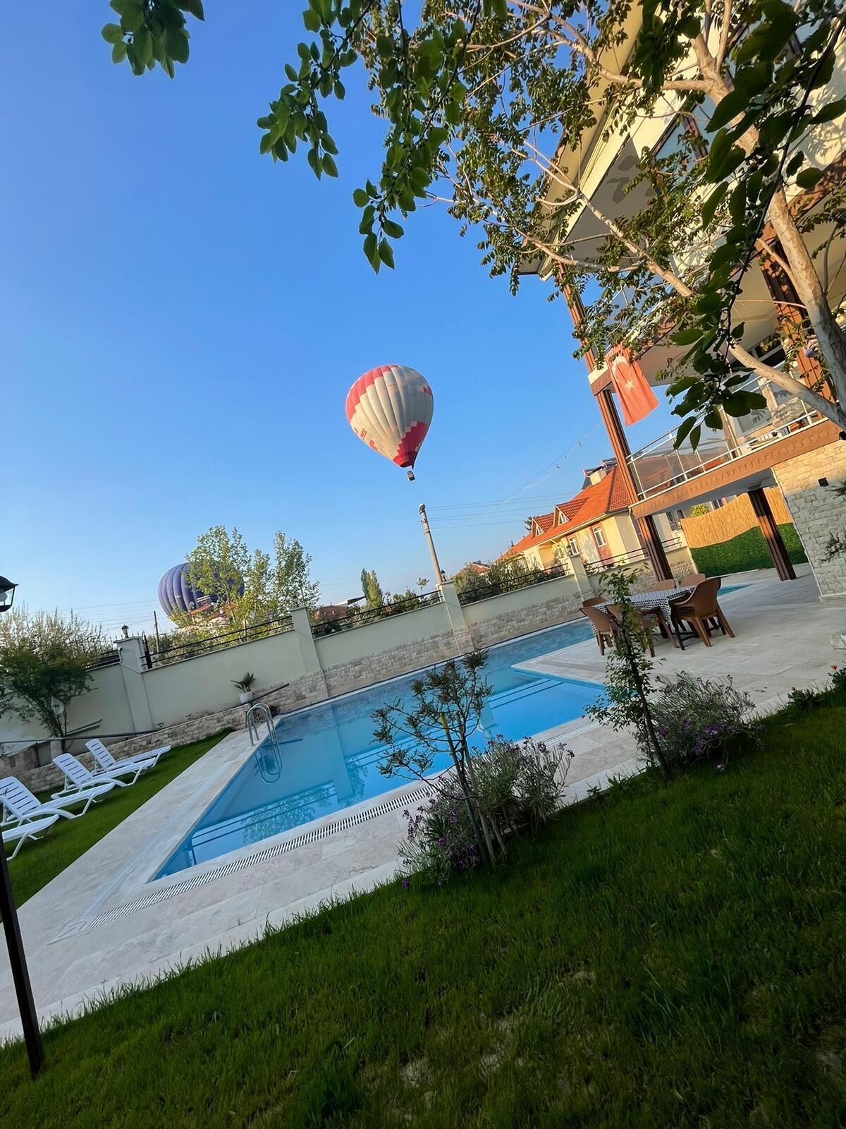 A swimming pool with lounge chairs, a hot air balloon in the background, and a building with a flag.