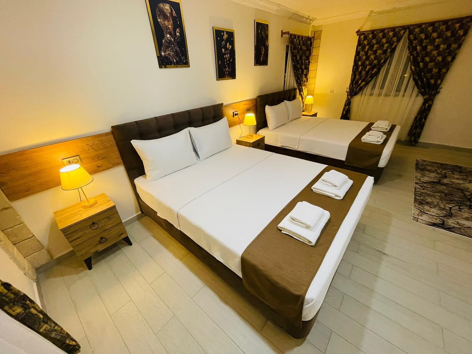A hotel room with two beds, a wooden headboard, a nightstand with a lamp, and a patterned rug.