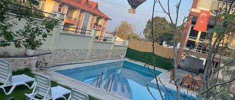 A swimming pool with lounge chairs, a hot air balloon in the background, and a building with a red roof.