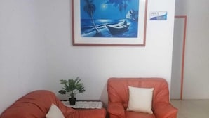 A room with two orange armchairs, a small table with a plant, and a framed painting of a boat on water. - Downtown  (San Andrés)