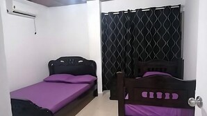 A small bedroom with a single bed, a nightstand, a window with a patterned curtain, and an air conditioning unit on the wall. - Downtown  (San Andrés)