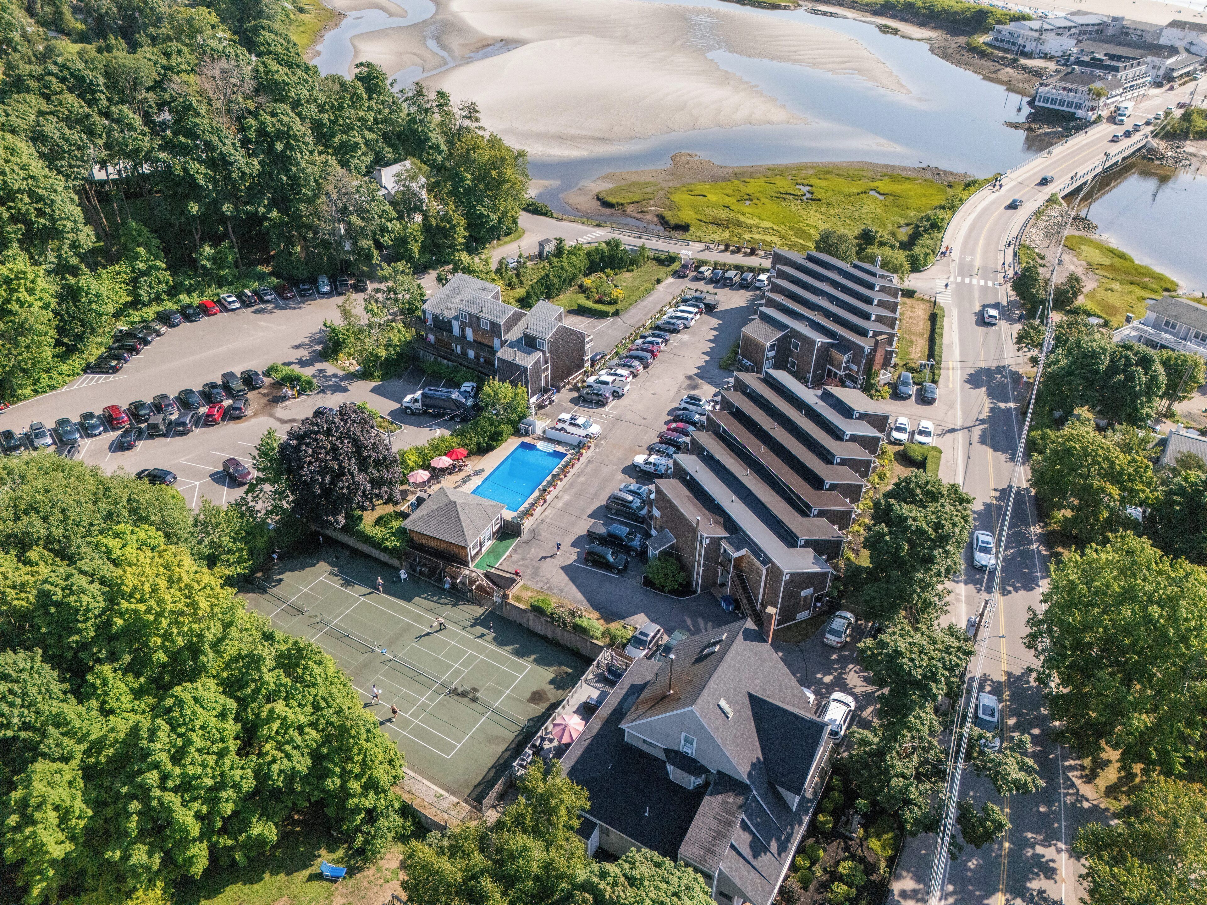 Vista aérea de una zona residencial con piscina, cancha de tenis y aparcamiento.