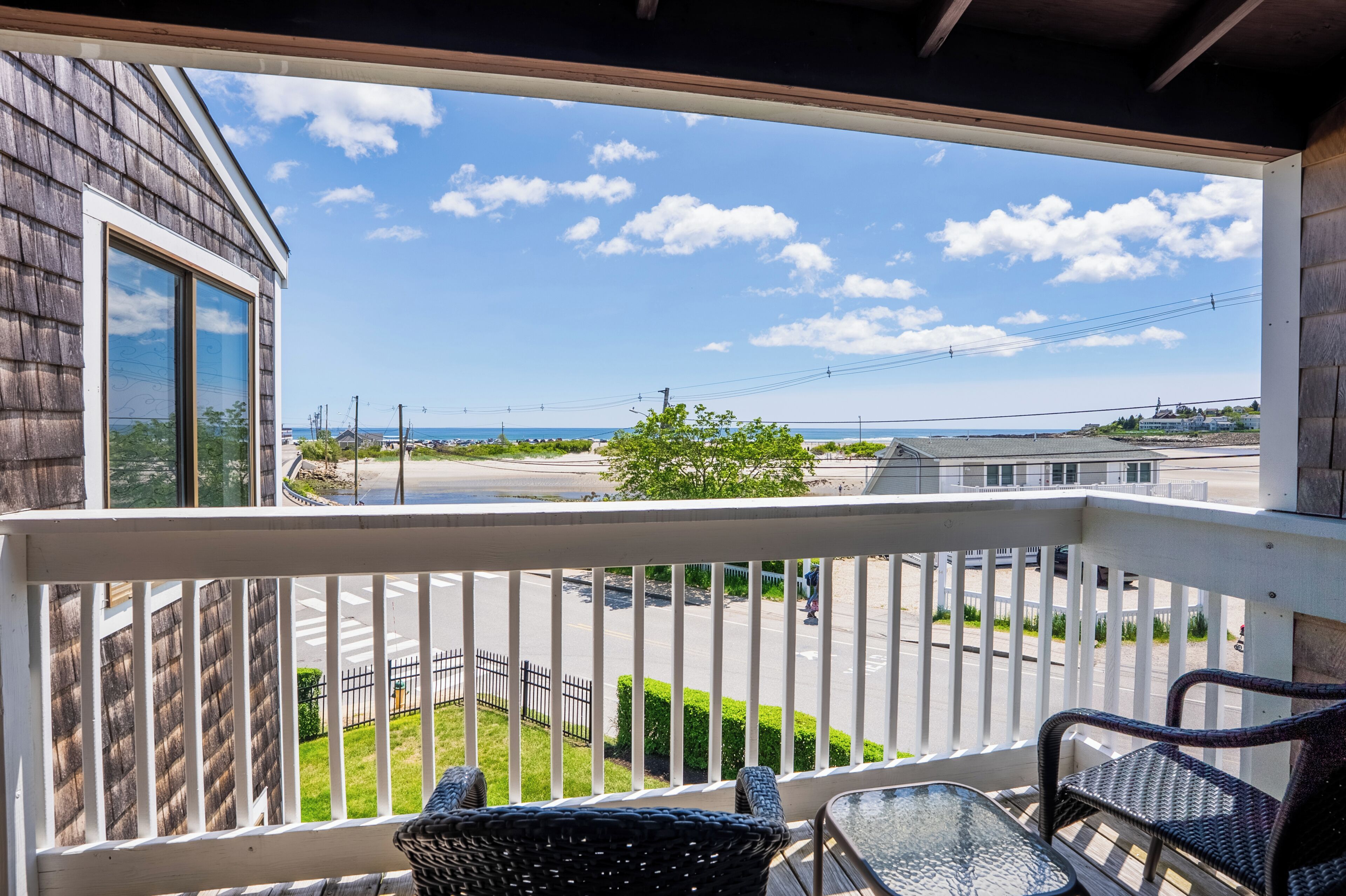 A balcony with wicker chairs, a glass table, and a view of a road and greenery.
