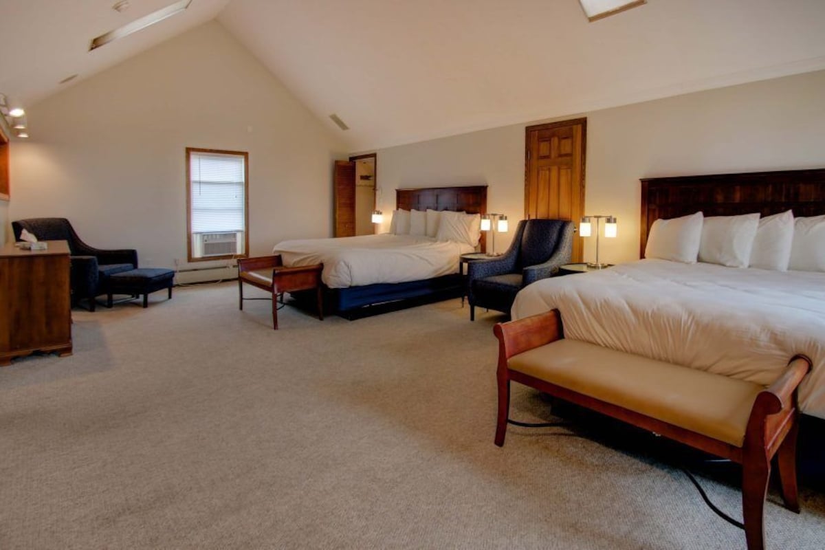 A hotel room with two beds, a desk, a chair, and a bench.
