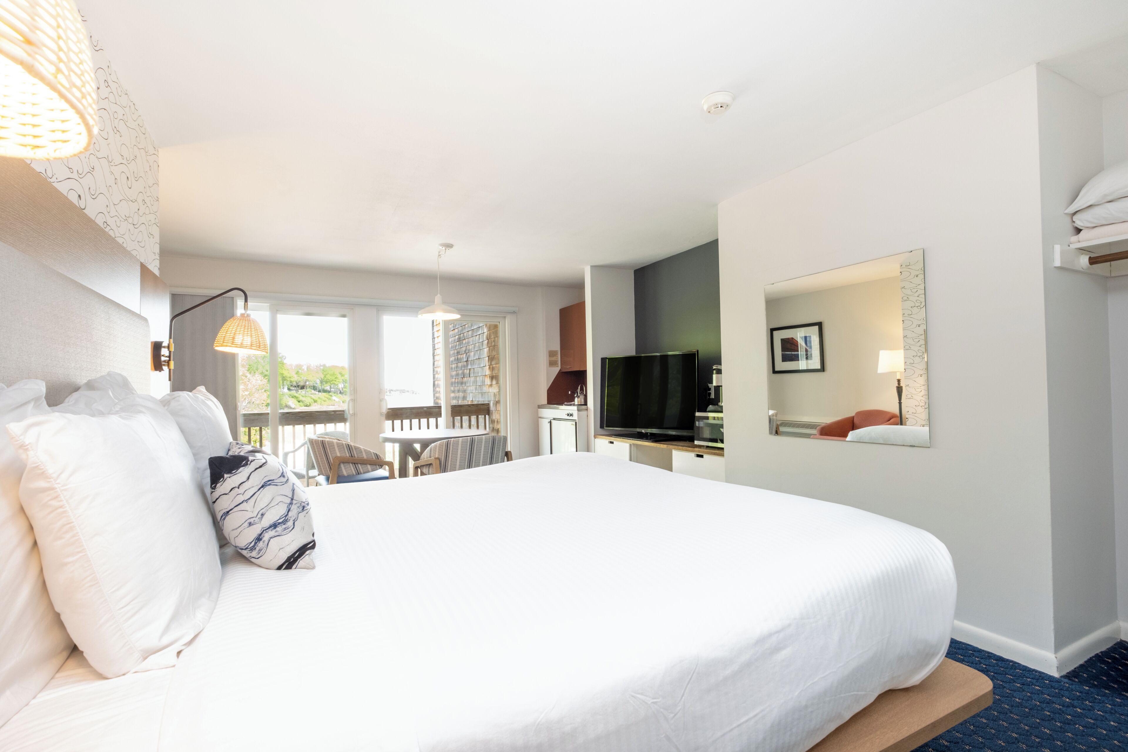 A hotel room with a large bed, a television, a dining area, and a balcony.