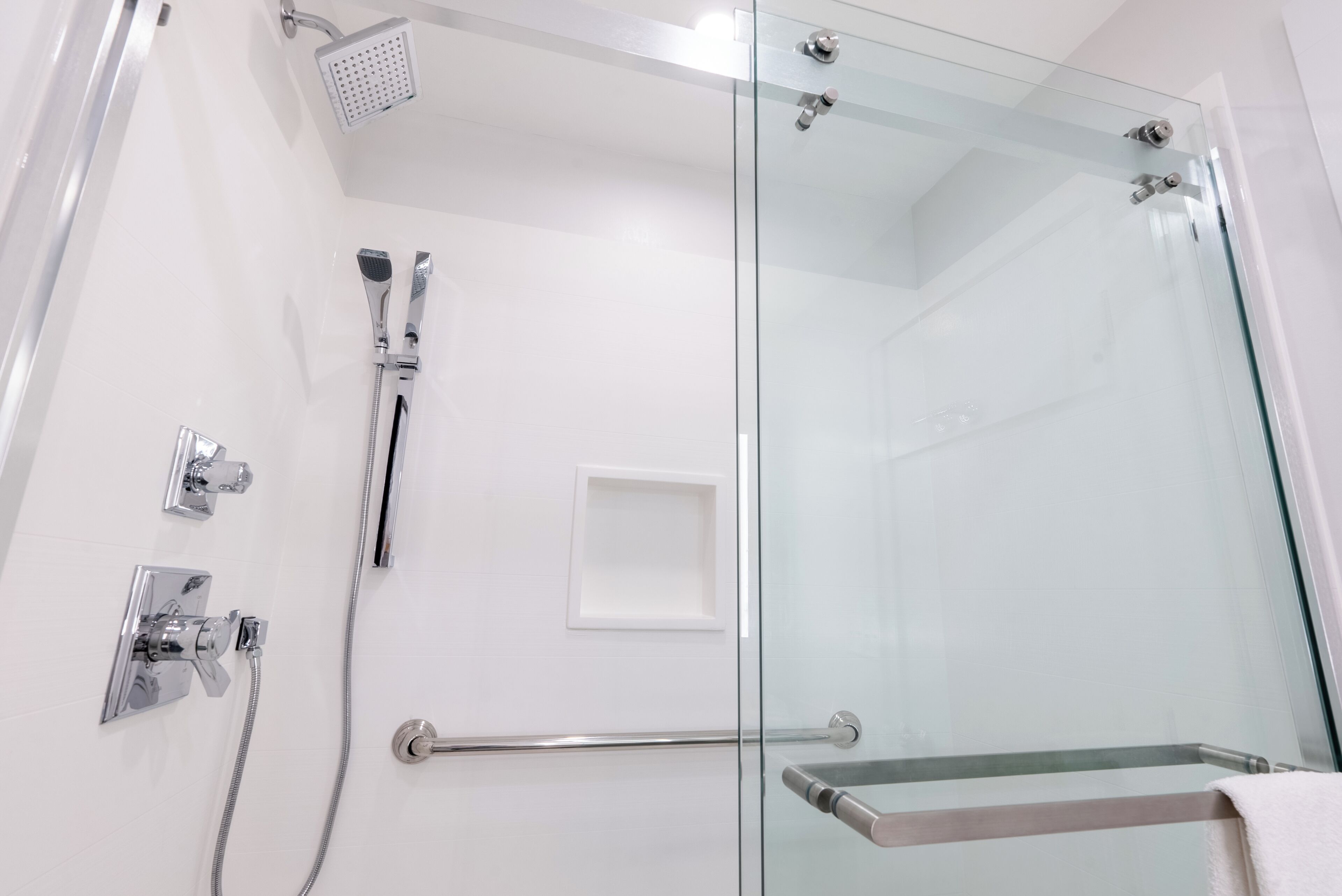 A modern bathroom with a glass shower enclosure, a handheld showerhead, a wall-mounted faucet, and a glass door with a towel rack.