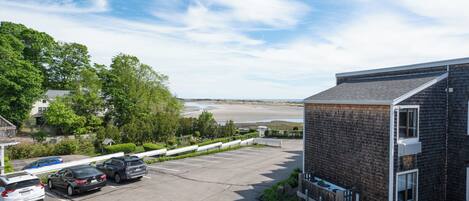 A parking lot with cars, a building with a sloped roof, and a view of a beach and water body.