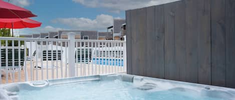A hot tub with a wooden fence, a pool, and a white railing.