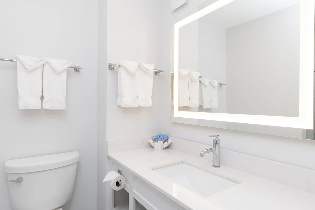 A modern bathroom with a white toilet, a sink with a mirror above it, and two towels hanging on the wall.