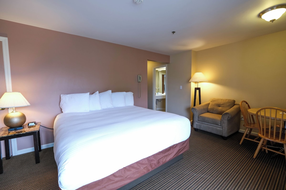 A hotel room with a large bed, a chair, a table, and a lamp.