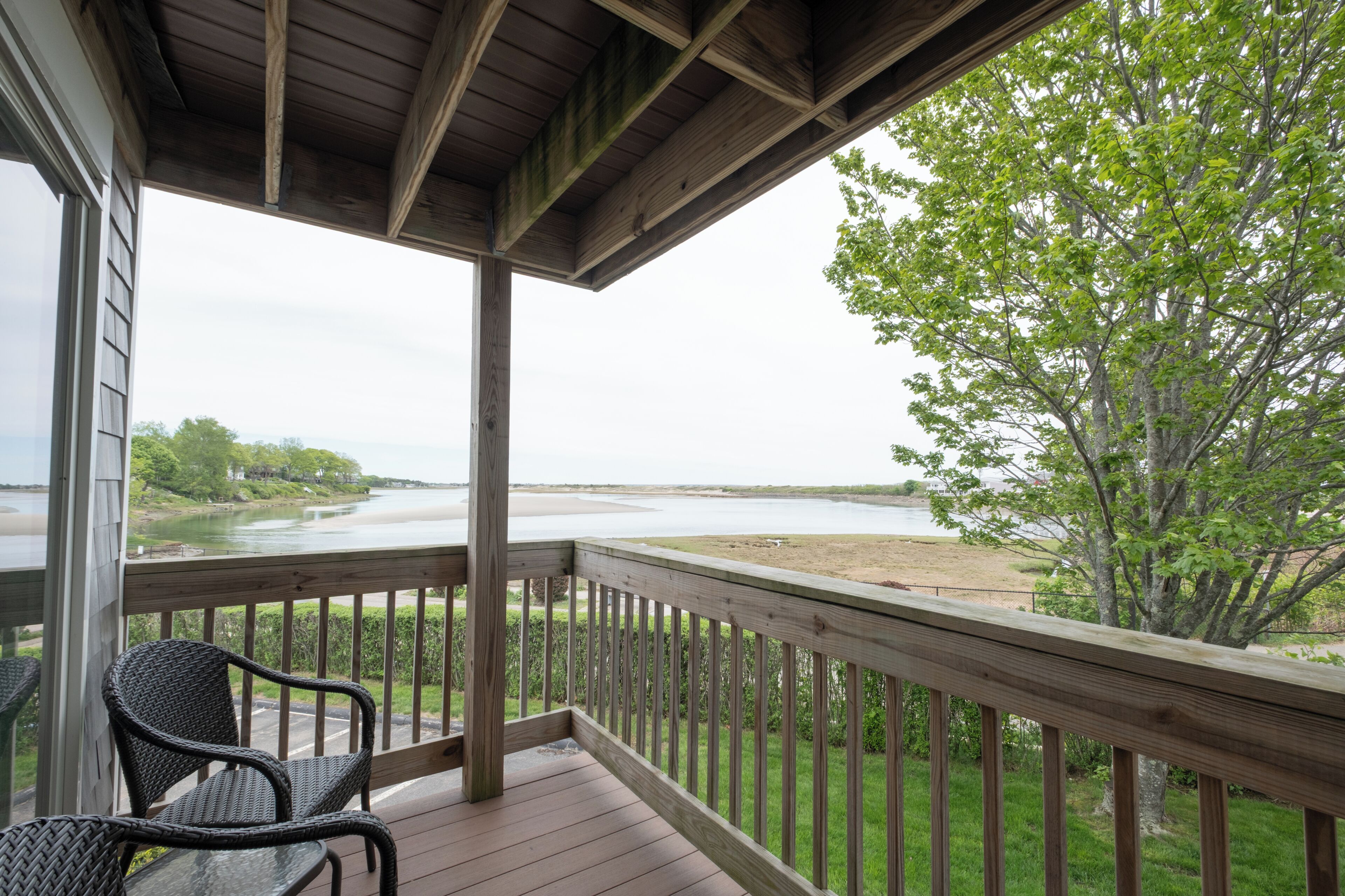 Une terrasse en bois avec une rambarde, une chaise en osier et une vue sur une rivière et une plage.