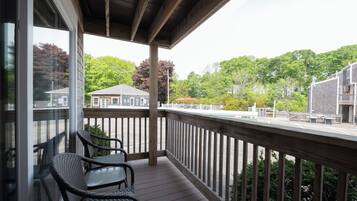 A covered balcony with wicker chairs, a wooden deck, and a view of a building and trees.