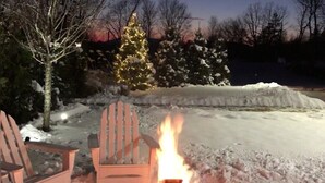 A snow-covered outdoor area with a fire pit, two Adirondack chairs, and a Christmas tree. - Hotel Dylan (Woodstock)
