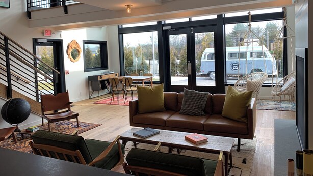 A spacious living area with a high ceiling, a sofa, chairs, a table, and a view of a van outside. - Hotel Dylan (Woodstock)