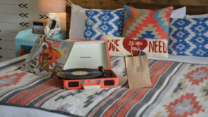 A bed with patterned bedding, a record player, a book, and decorative pillows. - Hotel Dylan (Woodstock)