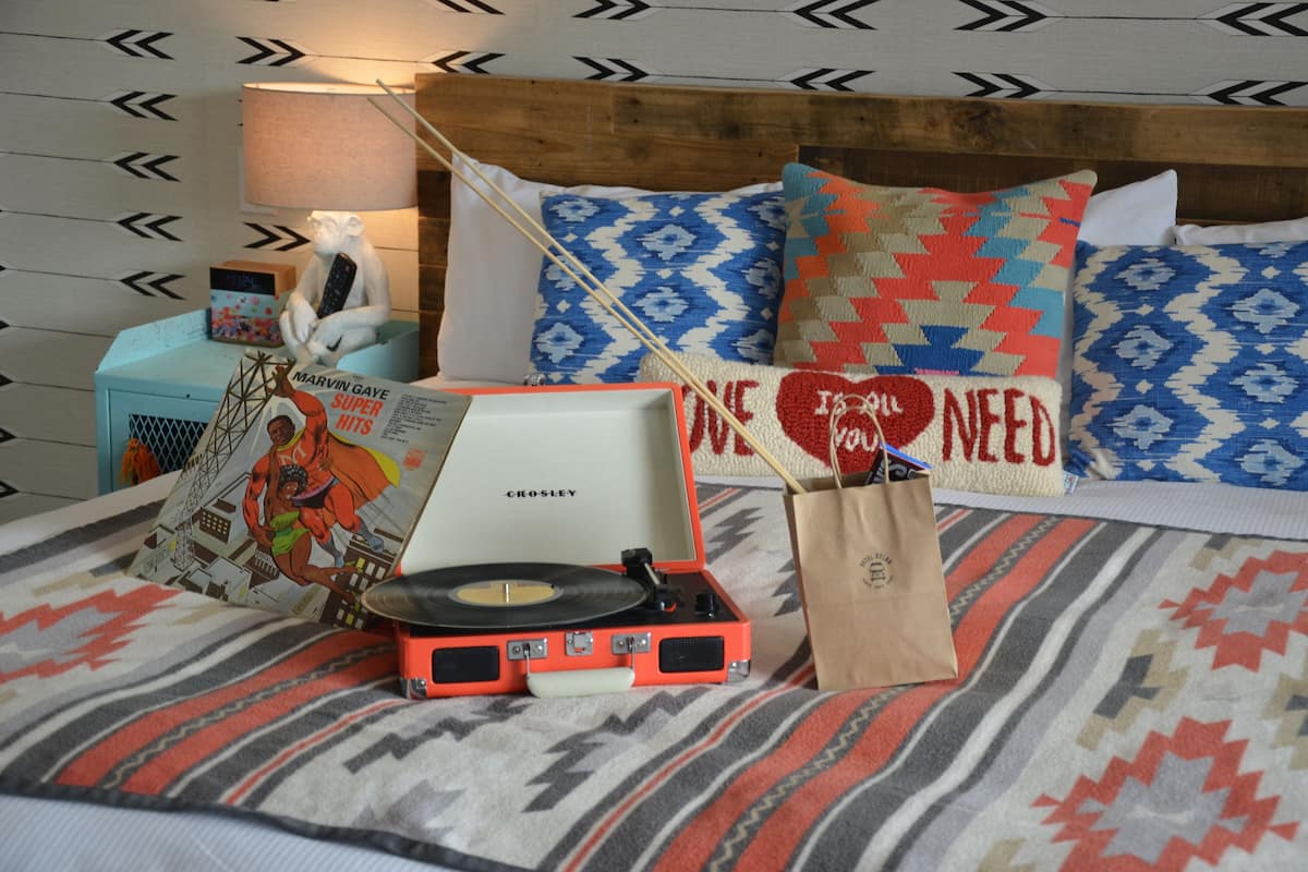 A bed with patterned bedding, a record player, a book, and decorative pillows.