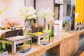 A buffet area with various food stations and decorative flowers. - Shenlong New World Hotel (Leiyang)