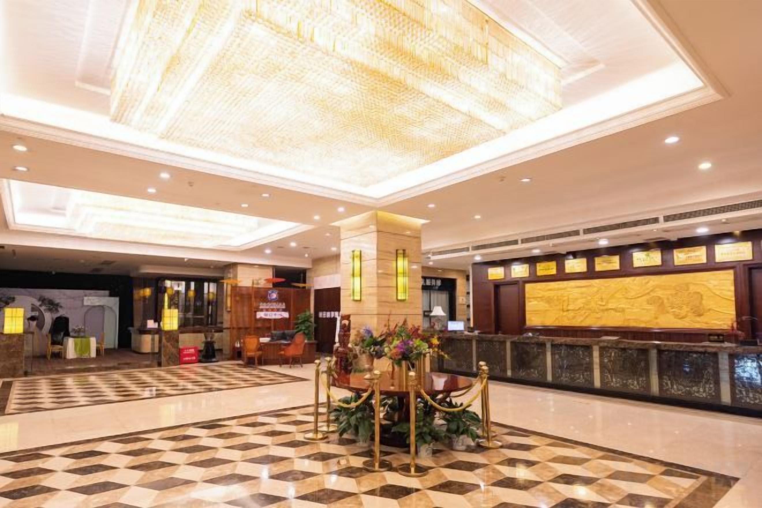 A hotel lobby with a checkered floor, a reception desk, and a chandelier.