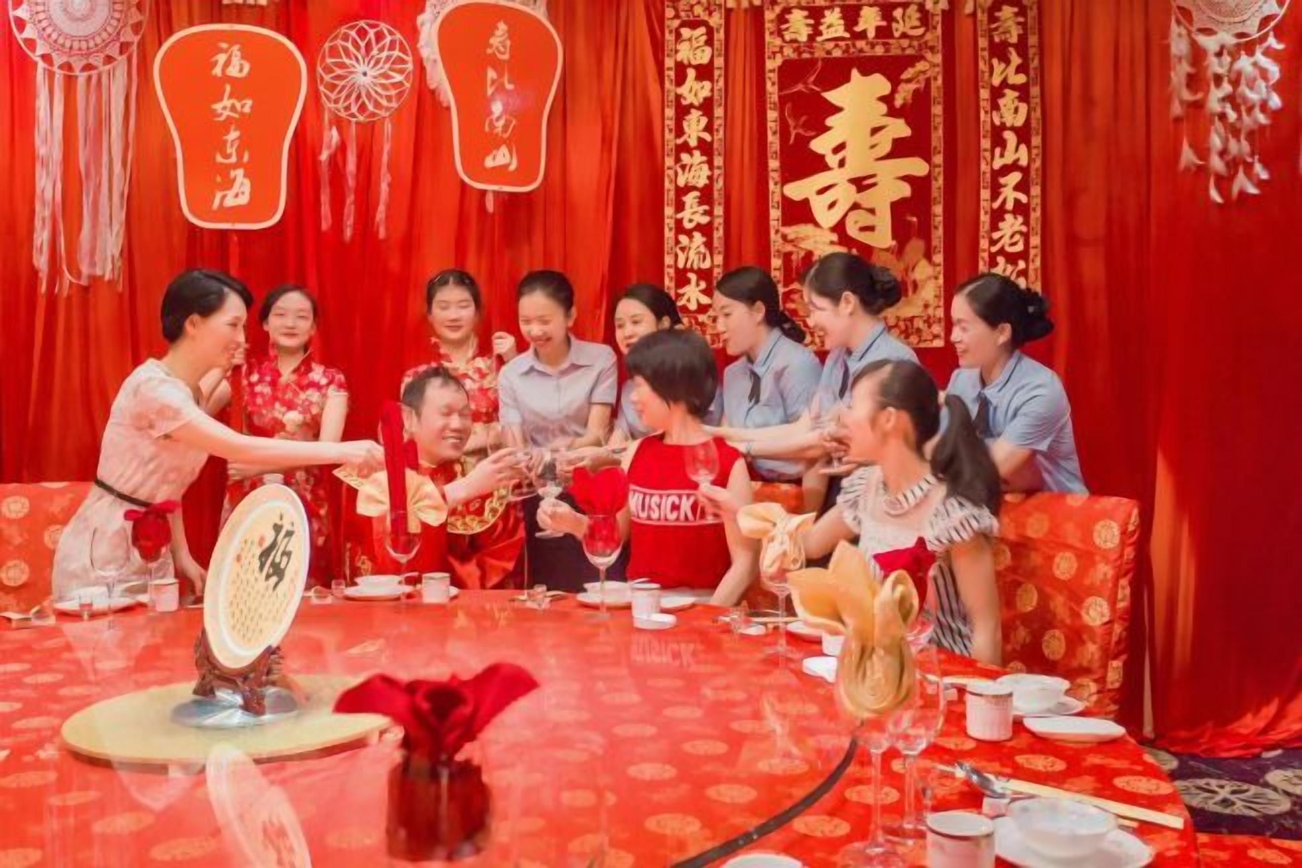 A group of people seated around a table with a red tablecloth, engaged in a game involving a paddle.
