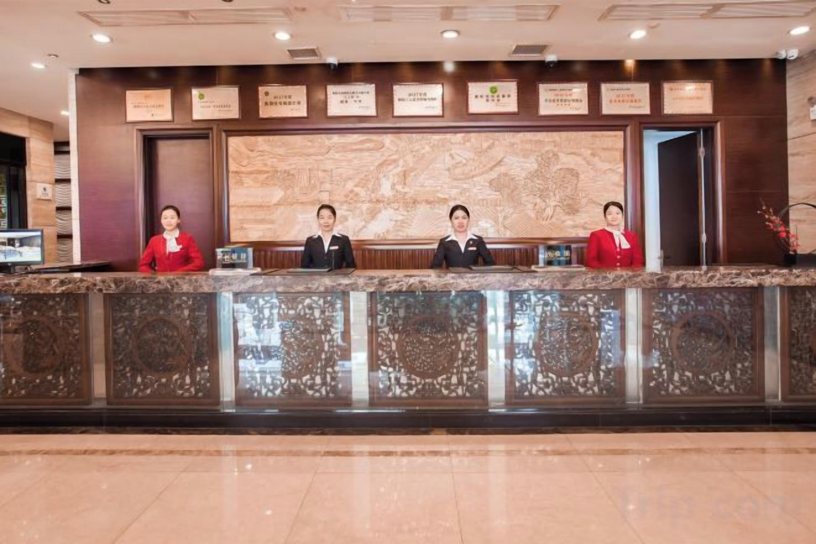 A reception desk with three staff members, a marble wall with plaques, and a polished floor.